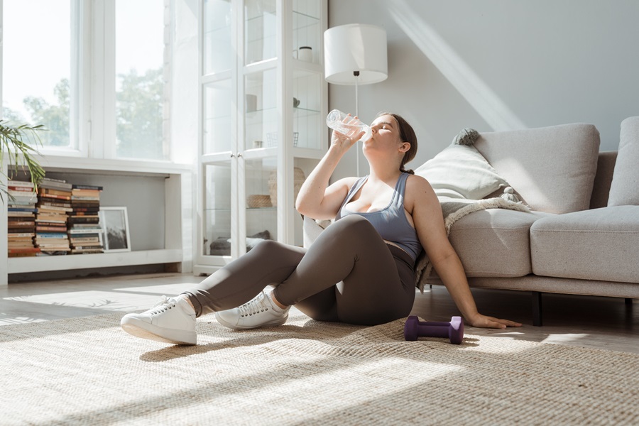 Weekly Jillian Michaels Workout Routines a Woman Drinking Water Wearing Workout Clothes Sitting on the Floor in Front of a Couch