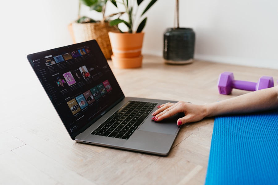 Weekly Jillian Michaels Workout Routines Close Up of a Person Pulling Up a Workout Video on a Laptop on a Wooden Floor with a Dumbbell and a Yoga Mat in View