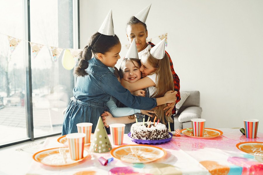 How to Set a Table for your Child's Birthday Party Kids Hugging Behind a Birthday Table with Party Hats On Their Heads