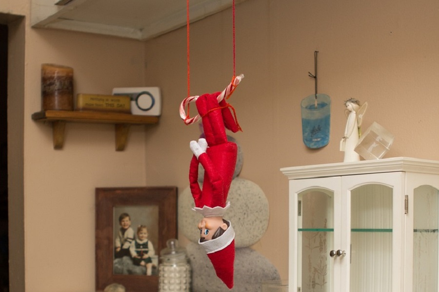 Introduce Elf on the Shelf Close Up of an Elf Hanging Upside Down from a Cabinet
