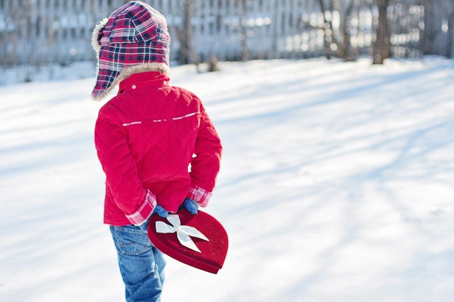 Disney Printables Little Boy Walking in the Snow with a Red Jacket on Holding a Heart Shaped Box of Chocolates Behind His Back