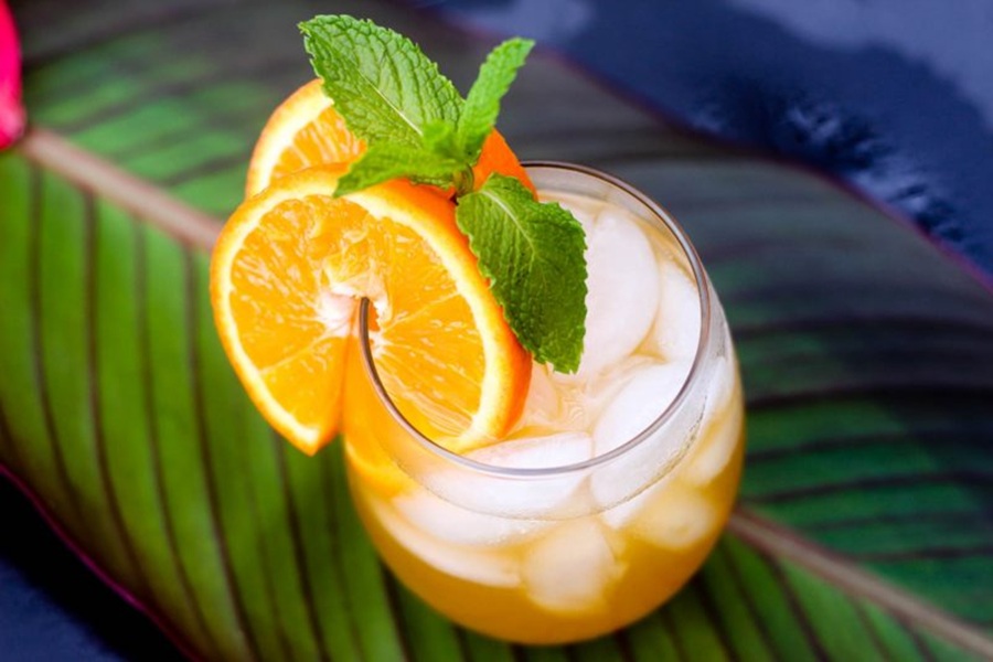 Easy Fireball Cocktail Recipe Sitting on a Tropical Leaf Garnished with Orange Slices and Mint Leaves