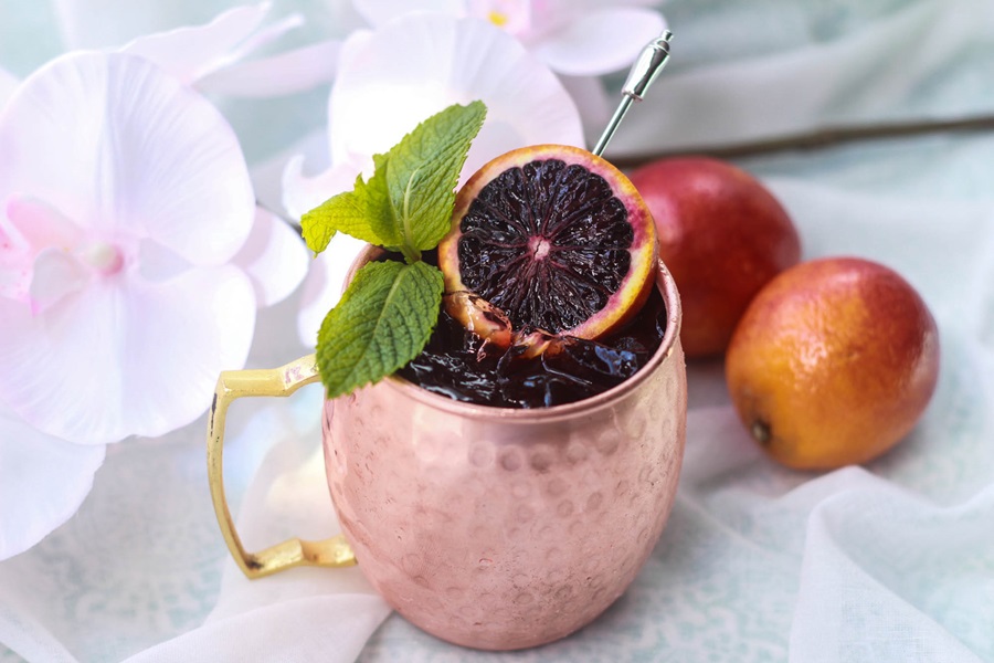 Blood Orange Moscow Mule Recipe for Pool Parties a Blood Orange Moscow Mule on a Table with Two Blood Oranges in the Background