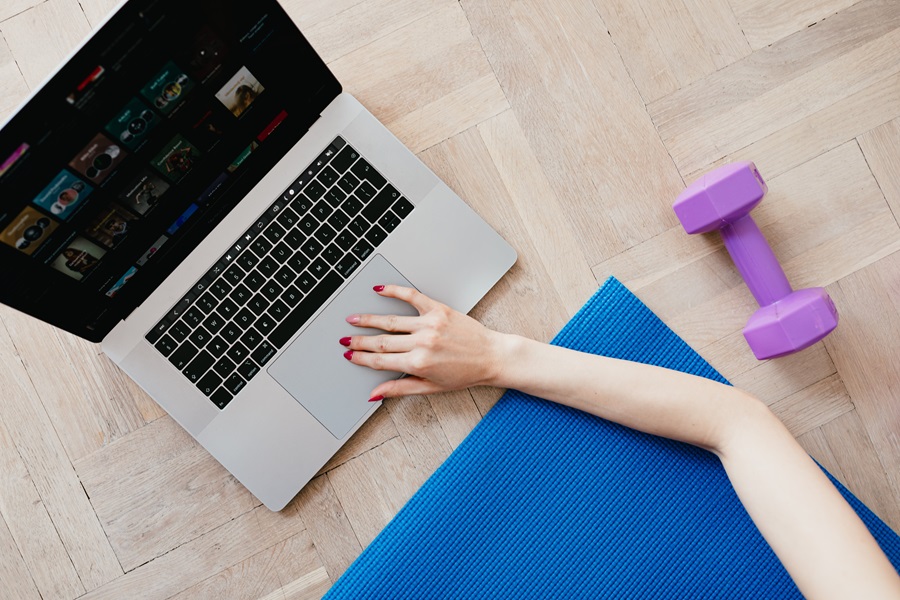 Core De Force Review Close Up of a Woman's Hand Using a Laptop on a Floor with a Dumbbell and a Yoga Mat in View
