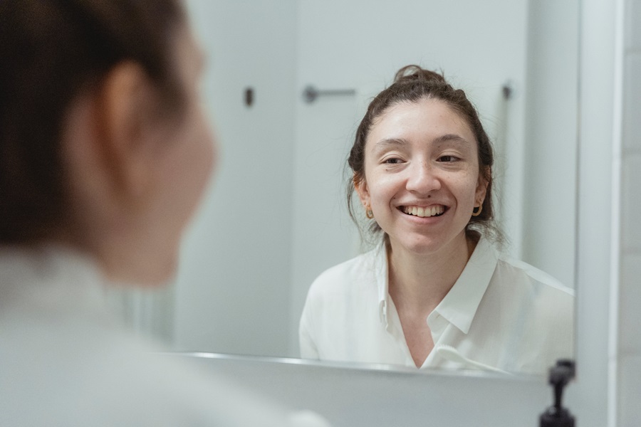 How to Whiten your Teeth at Home a Woman Smiling and Looking in a Mirror in Her bathroom