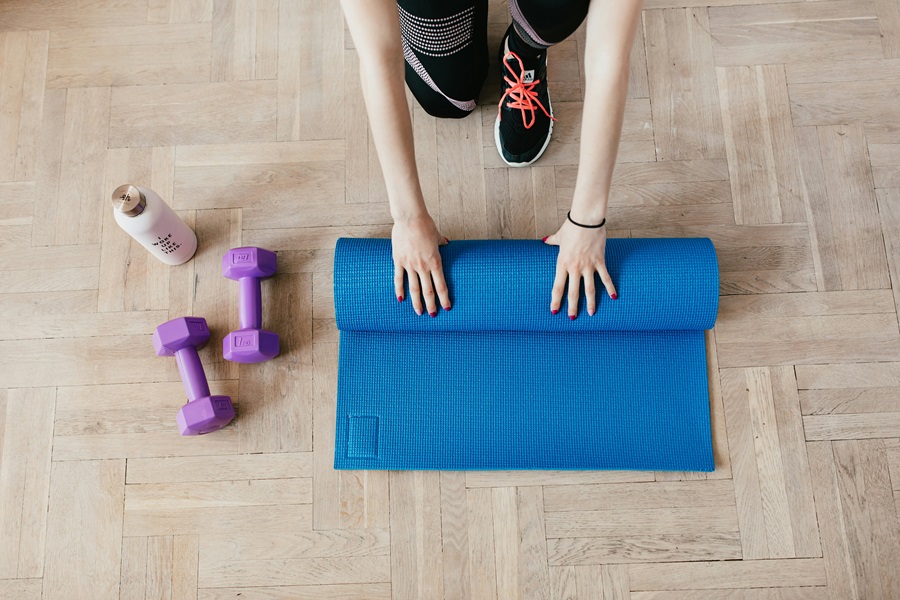 Shaun Week Workouts Close Up of a Woman Rolling Up a Yoga Mat with Two Dumbbells Next to it
