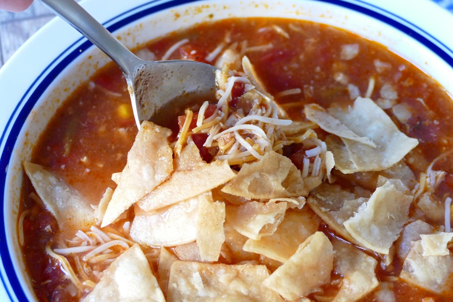 Easy Crock Pot Chicken Tortilla Soup Recipe Close Up of Tortilla Chips in a Bowl of Chicken Tortilla Soup with Shredded Cheese