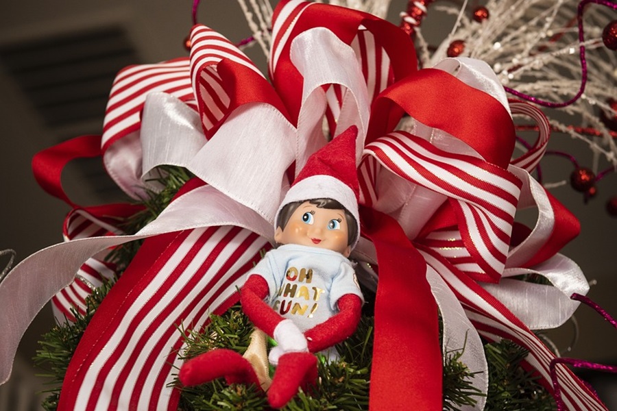 Welcome Back Elf on the Shelf Ideas Close Up of an Elf Resting in Christmas Ribbon, Red and White