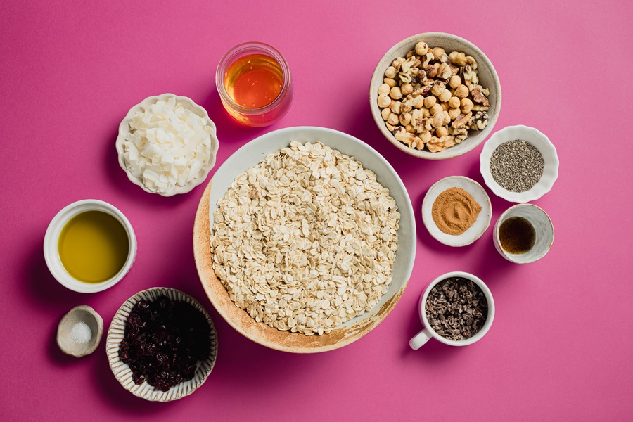 Easy Vegan Granola Recipe Ingredients Separated Into Small Bowls on a Pink Surface