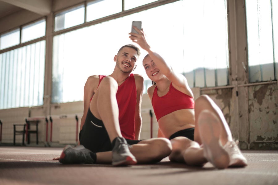 Daily Exercises to Get Rock Hard Abs a Man and a Woman in Matching Workout Clothes Sitting on the Ground Taking a Selfie Together