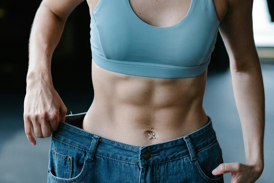 Daily Exercises to Get Rock Hard Abs Close Up of a Woman Wearing a Blue Sports Bra Holding Up Jeans That Are Too Big for Her