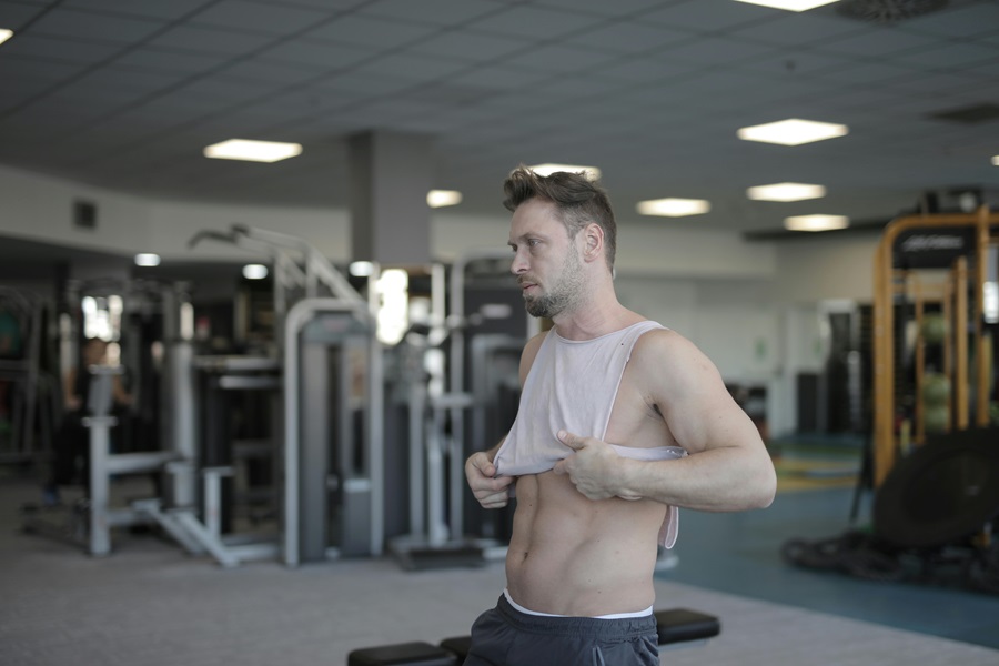 Daily Exercises to Get Rock Hard Abs a Man Sitting in a Gym Pulling His Shirt Down Showing Abs