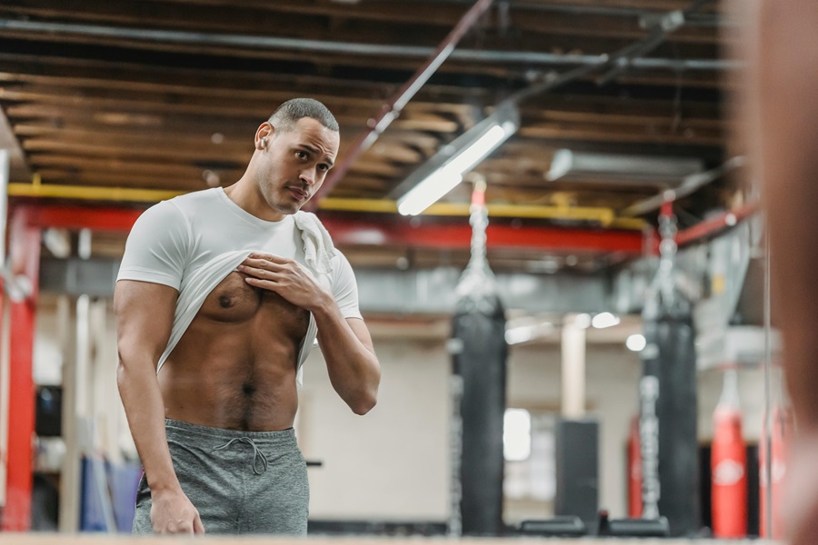 Daily Exercises to Get Rock Hard Abs a Man Standing in a Gym Lifting His Shirt to Look at His Abs