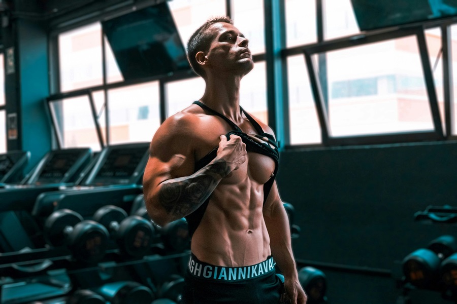 Daily Exercises to Get Rock Hard Abs a Man in a Gym Lifting His Tank Top to Look at His Abs