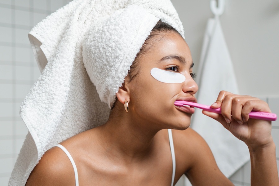 Exercises to Do While Brushing Your Teeth a Woman Wearing Her Hair in a Towel and Eye Patches Under Her Eyes Brushing Her Teeth