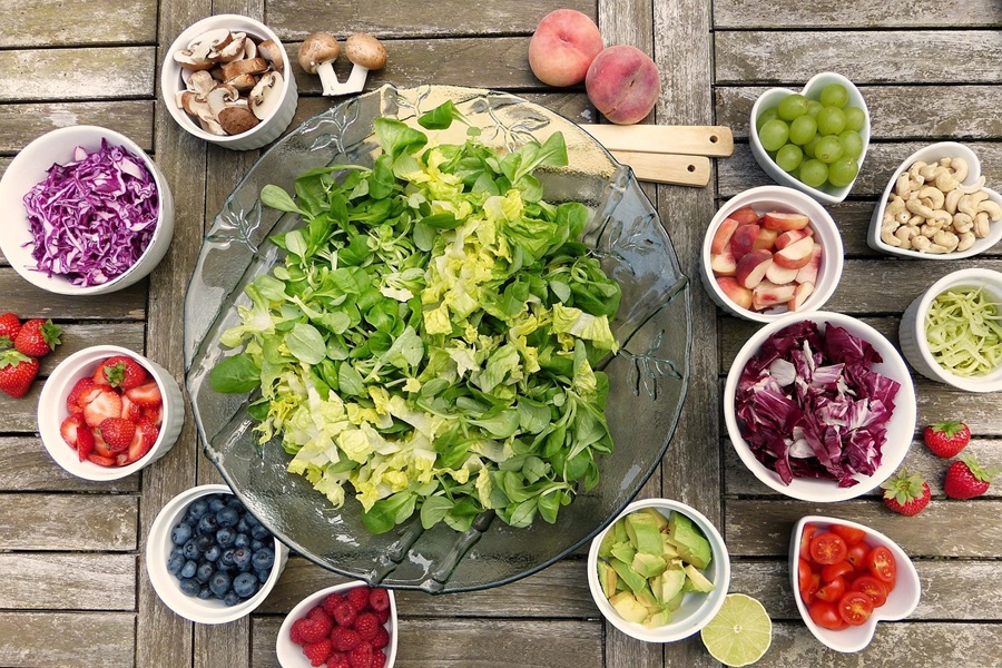 Keto Carb Limit vs Low Carb Limit a Glass Bowl Filled with Lettuce Surrounded with More Small Bowls Each with a Different Fruit or Veggie to Add to the Salad