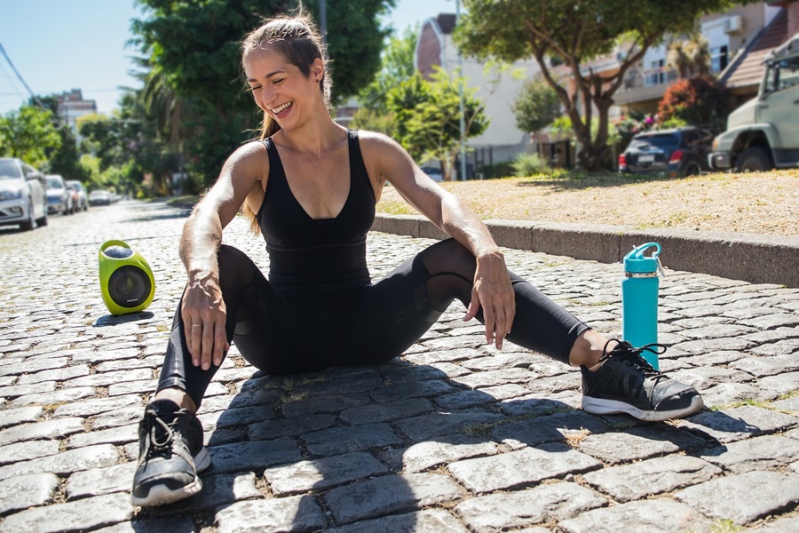 Transform 20 BONUS with Weights, Workouts, and Tips a Woman Wearing Workout Clothes Sitting on the Ground Smiling, Next to a Water Bottle and a Bluetooth Speaker