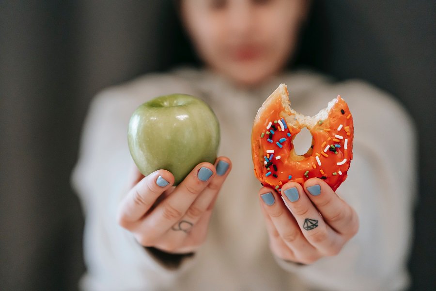 How to Get Through Hunger When Fasting a Woman Holding Up an Apple in One Hand and a Donut in the Other With a Bite Out of the Donut