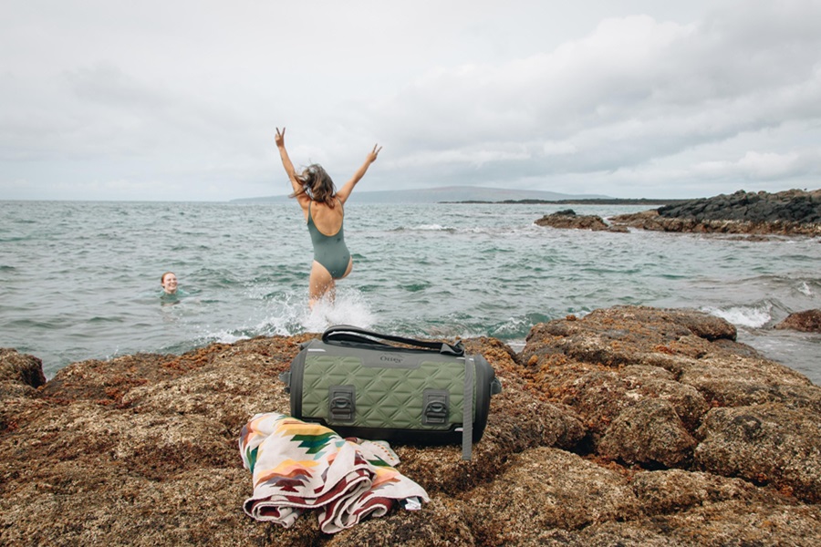 Otterbox Trooper Coolers Features and Review a Woman Jumping into an Ocean with a Cooler in the Foreground