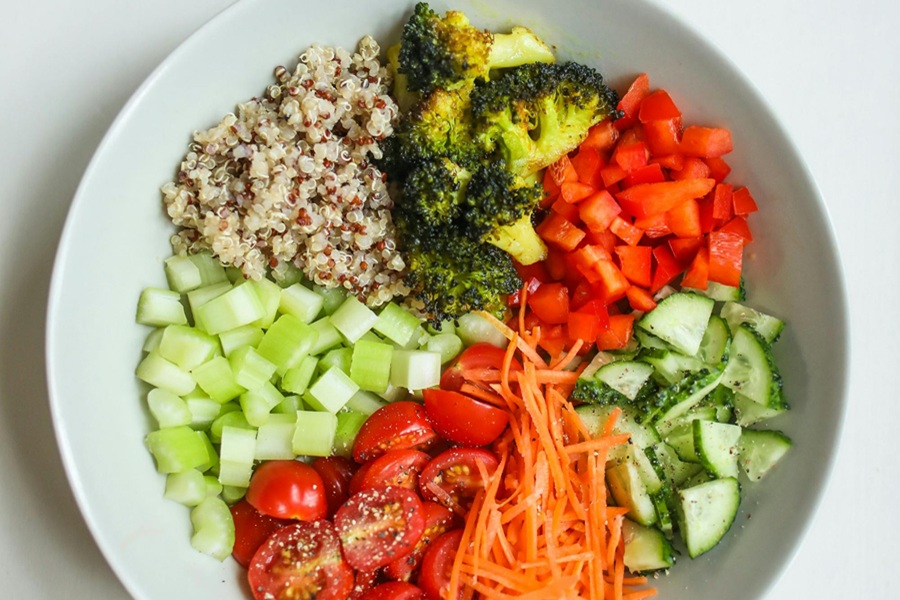 Low Carb Buddha Bowl Recipes Close Up of Broccoli, Bell Peppers, Tomatoes, Cucumbers, and Quinoa in a White Bowl