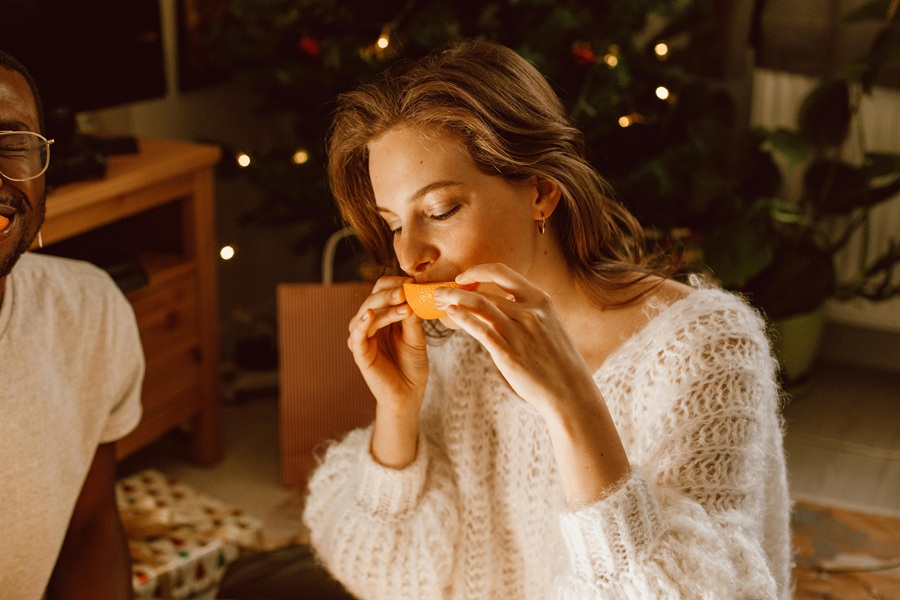 Low-Carb Holiday Recipes a Woman Dressed Nicely Eating an Orange Slice with a Christmas Tree in the Background