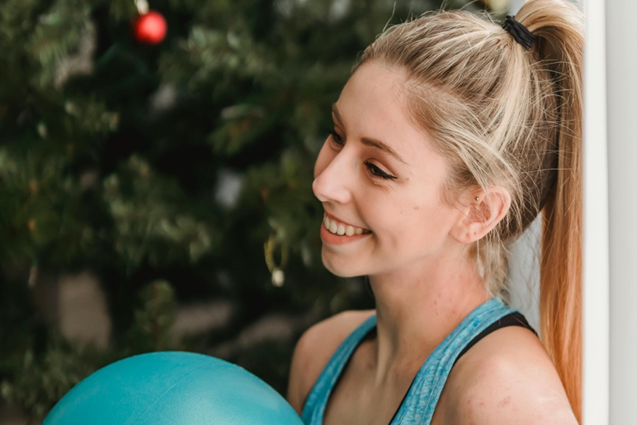 Low-Carb Holiday Recipes a Woman Wearing Workout Clothes and Holding a Medicine Ball Sitting Against a Wall with a Christmas Tree in the Background