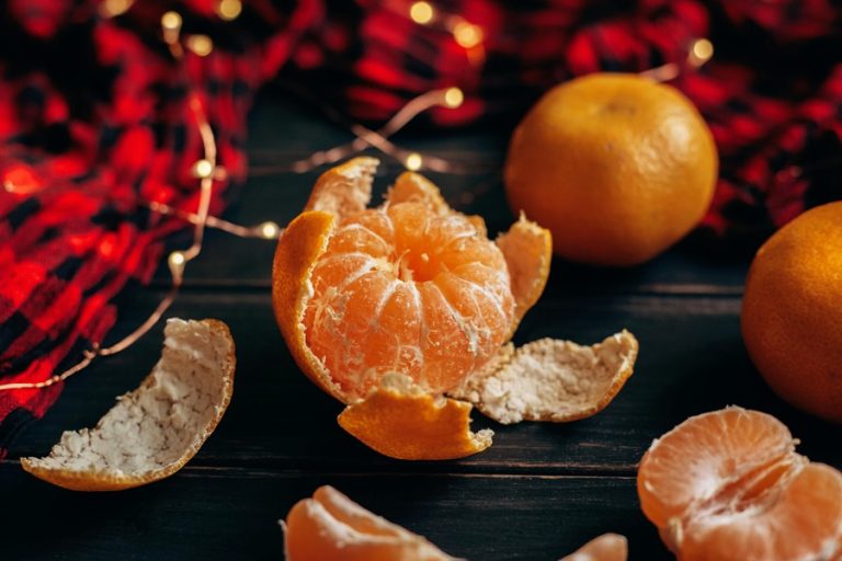 Low-Carb Holiday Recipes Close Up of a Partially Peeled Orange on a Wooden Surface with Small Christmas Fairy Lights in the Background