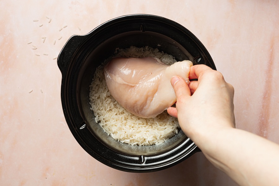 Salsa Chicken and Rice Recipe Raw Chicken Breast Being Placed On Top of Rice in a Crockpot