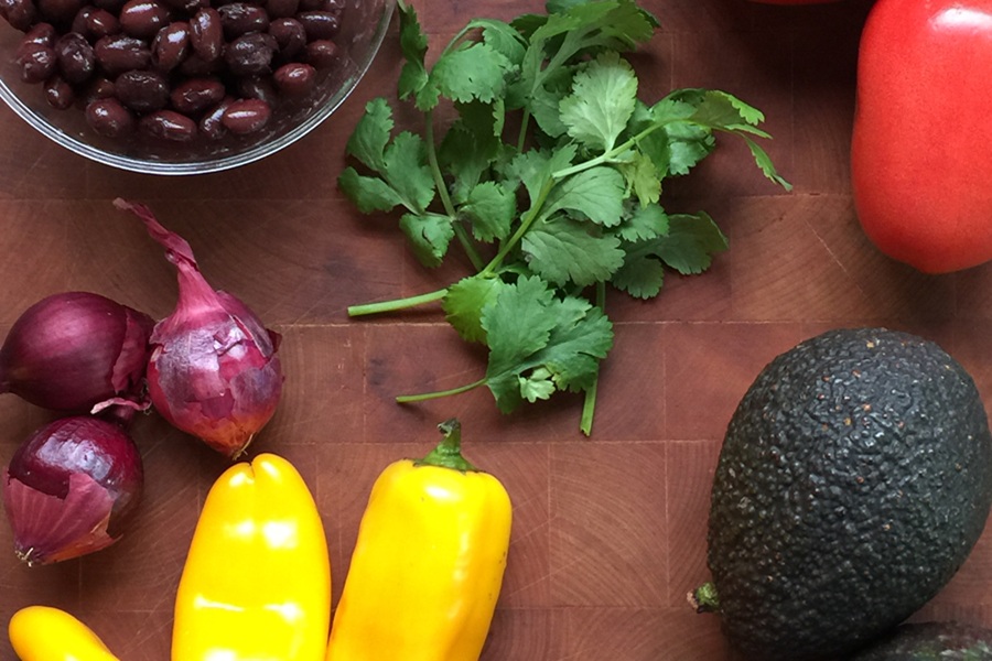 Easy Low Carb Cowboy Caviar Recipe Ingredients on a Wooden Surface Including Peppers, Cilantro, Beans, Onions, and Avocados