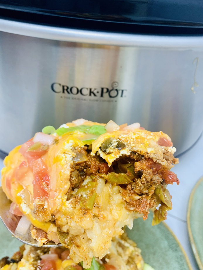 Slow Cooker John Wayne Casserole with Tater Tots Serving the Casserole in Front of a Crockpot
