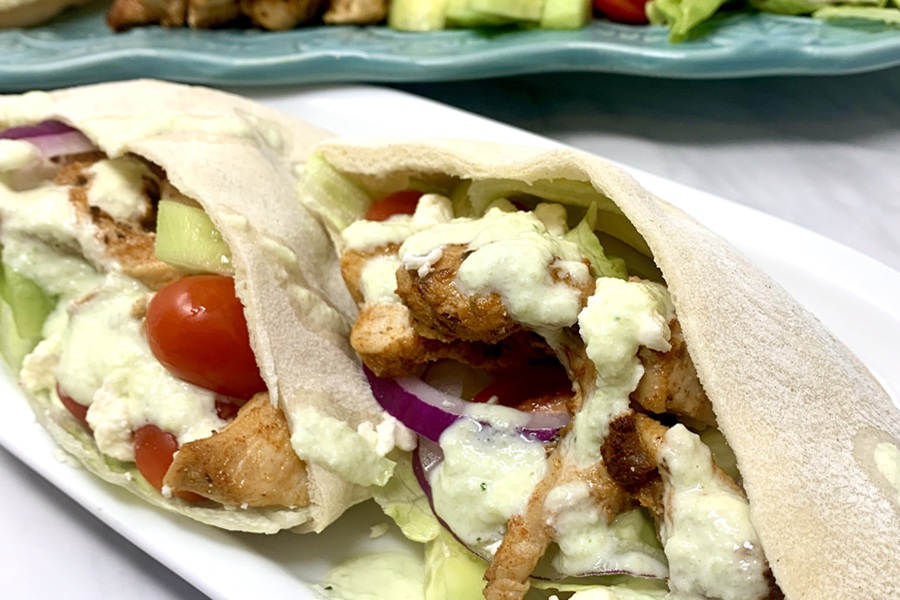 Chicken and Tzatziki in Pita Pockets on a Plate Next to a Serving Platter of Ingredients in Neat Rows