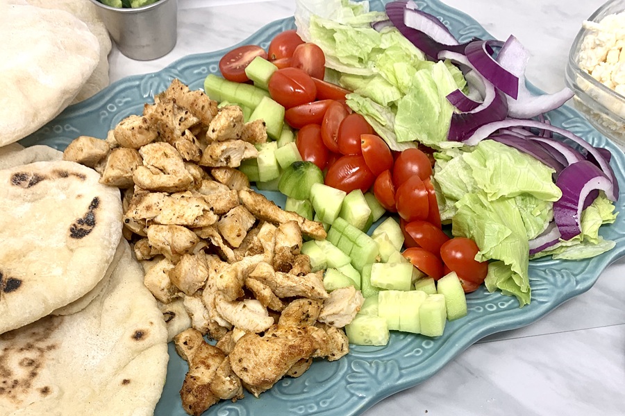 Chicken and Tzatziki in Pita Pockets a Serving Platter of Ingredients in Neat Rows including Chicken, Tomatoes, Lettuce, Red Onions, and Pita Bread