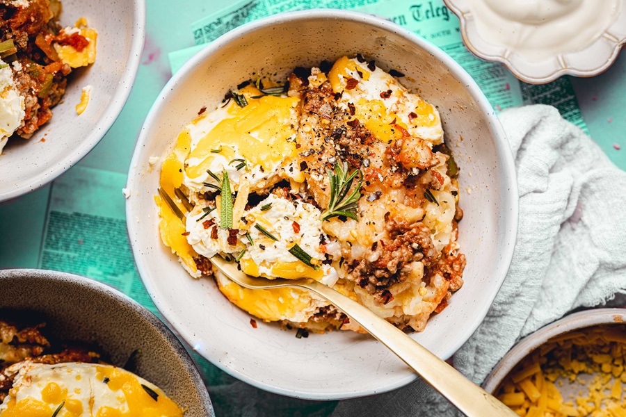 Slow Cooker John Wayne Casserole with Tater Tots Overhead View of a Bowl of Casserole with a Spoon and Ingredients Next to It