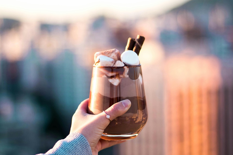 Spiked Hot Chocolate Recipes a Person Holding Up and Out a Cup of Hot Chocolate Topped with Marshmallows While Standing Outside 