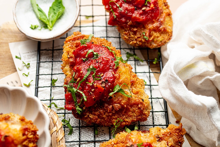 Best Panko Chicken Parmesan Recipe Chicken Breasts Topped with Sauce and Basil Leaves on a Wire Rack Over a Paper Towel