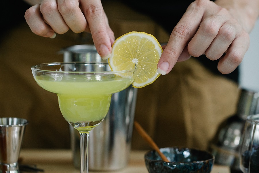 Margarita Pitcher Recipes that are Perfect for Parties Close Up of a Bartender Placing a Lemon Slice on the Rim of a Margarita Glass