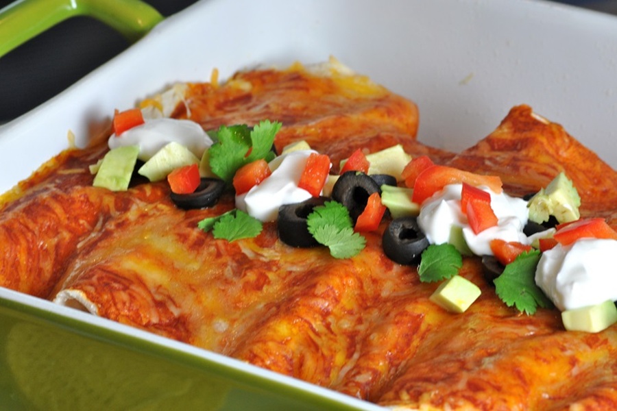 Easy Chicken Enchiladas Recipe Enchiladas Topped with Guacamole, Sour Cream, Tomatoes and Olives in a Baking Dish