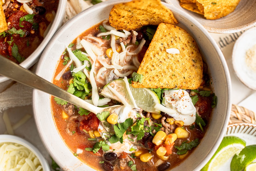 Easy Crockpot Taco Soup Recipe Close Up of a Bowl of Soup Topped with Lime, Cheese, Cilantro, and Chips