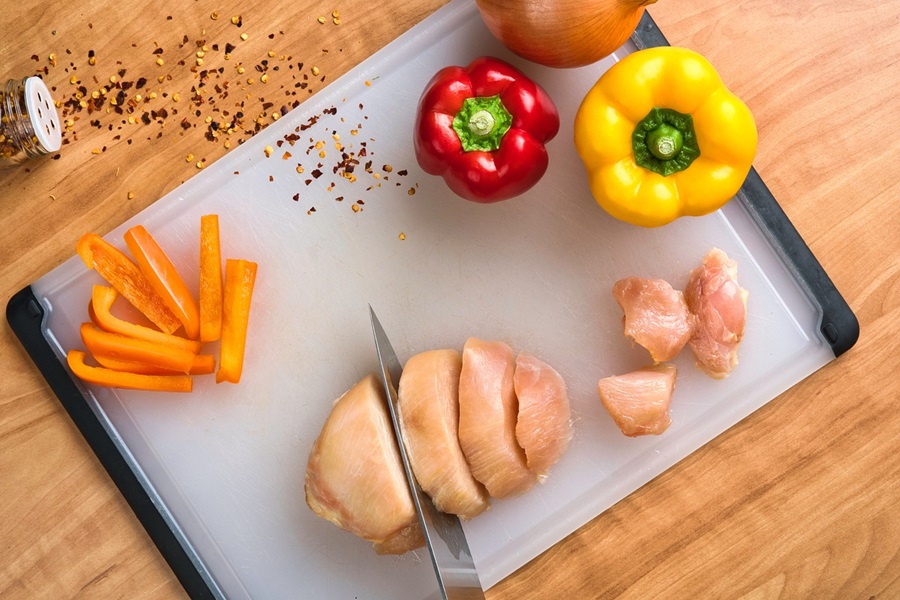 Meal Prep Recipes for Lunch Made with Chicken Chicken Breasts, Bell Peppers, and Carrots on a Cutting Board with a Knife in the Chicken Breast