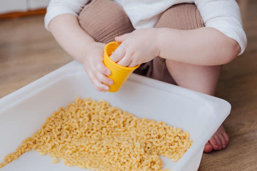 Macaroni and Cheese Recipes for a Crowd Close Up of a Young Child Playing with Raw Macaroni Noodles