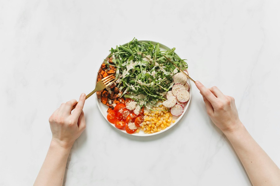 Master Your Metabolism Reviews and What's to Love Close Up of a Plate of Salad with a Person's Hands in View 