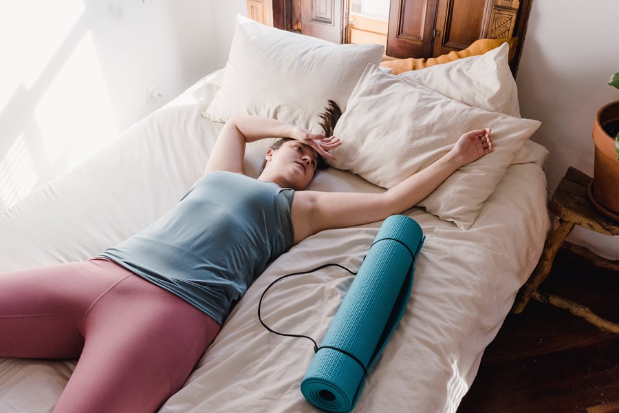 Morning Meltdown 100 Tips and Tricks a Woman Laying on a Bed With Her Arm Over Her Forehead Next to a Rolled Up Yoga Mat