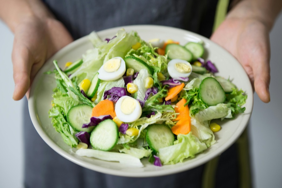 Whole30 vs Paleo vs Keto Close Up of a Salad Bowl Filled with Fresh Salad Being Held by a Person Wearing a Jean Apron