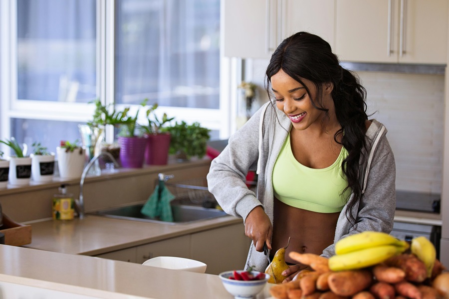 Whole30 vs Paleo vs Keto a Woman Wearing Workout Clothes Putting Together a Bowl of Fruit in a Kitchen