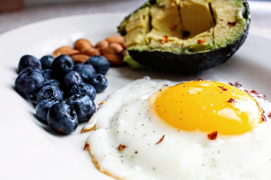 Tips for a Low Carb Diet Close Up of an Over Easy Egg with a Half an Avocado, Blueberries and Almonds