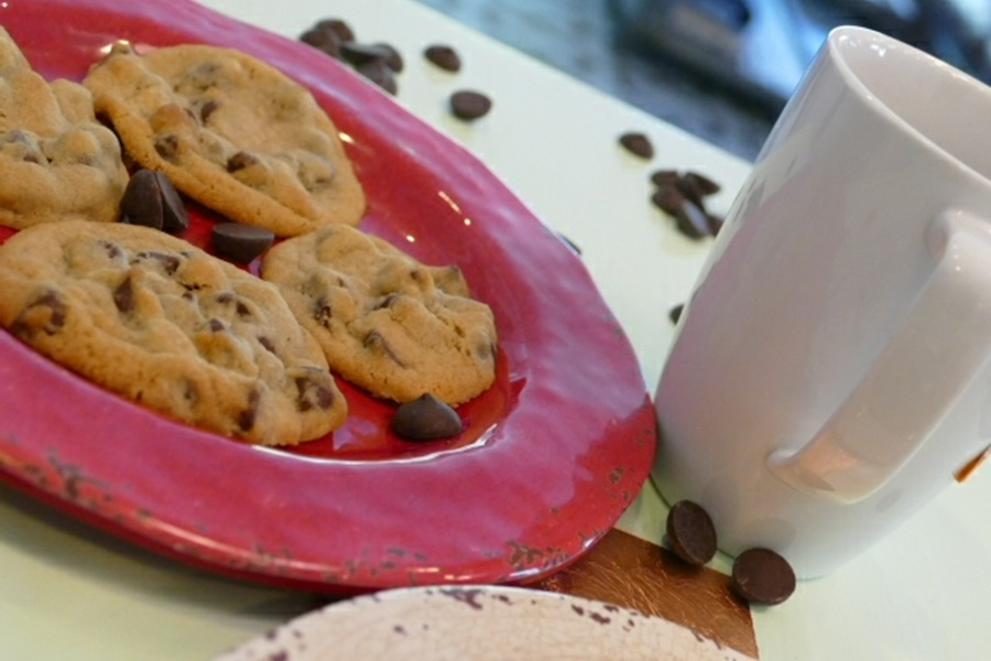 Ultimate Chocolate Chunk Cookie Recipe Cookies on a Red Plate Next to a Coffee Mug and Chocolate Chips Scattered Around