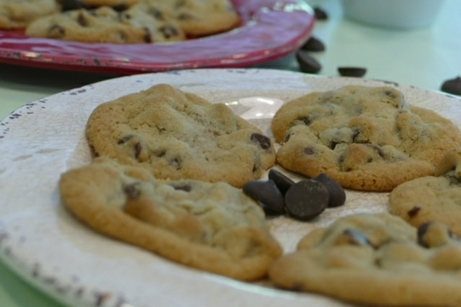 Ultimate Chocolate Chunk Cookie Recipe Cookies on a White Plate in the Foreground and on a Red Plate in the Background with Chocolate Chips Scattered Around