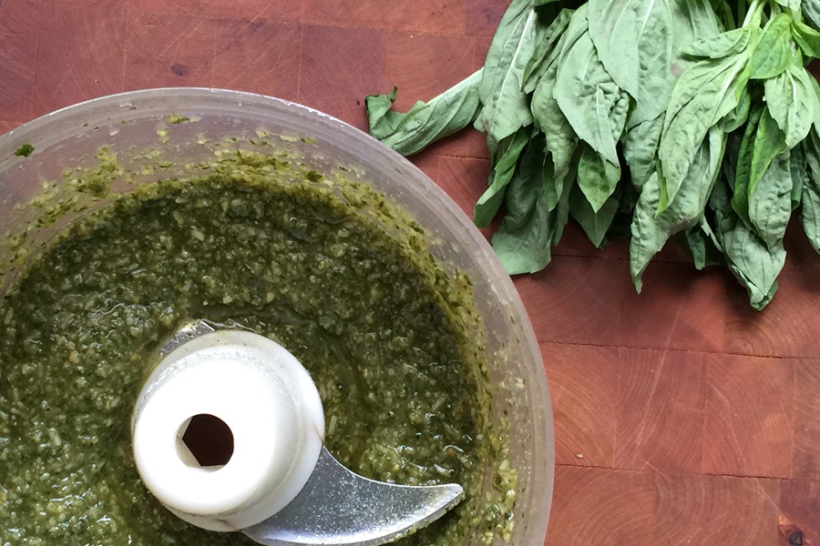 Basil Pesto Pasta Salad Recipe a Food Processer Filled with Pesto Sauce Next to a Bundle of Basil Leaves