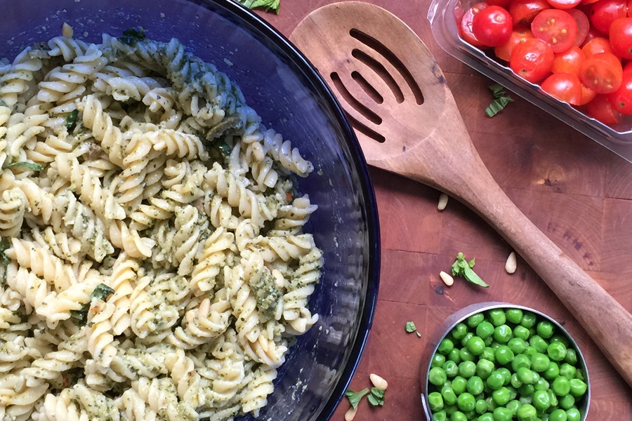 Basil Pesto Pasta Salad Recipe Overhead View of a Bowl of Pasta Next to a Small Dish of Peas and Another Small Dish Filled with Tomatoes