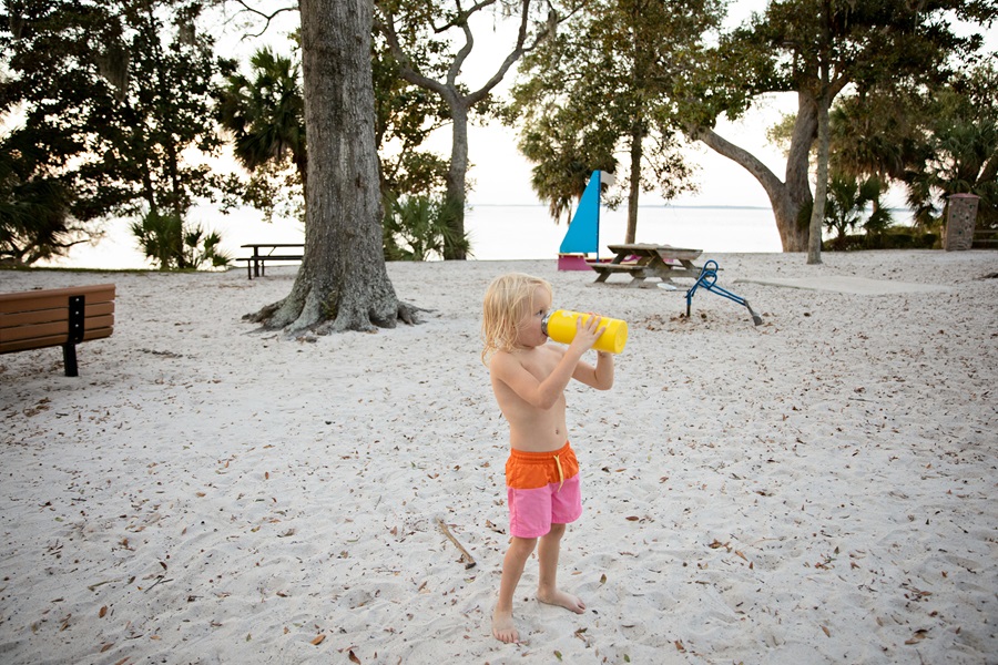 Beach Bag Essentials a Young Boy Standing on a Beach Drinking From a Reusable Water Bottle
